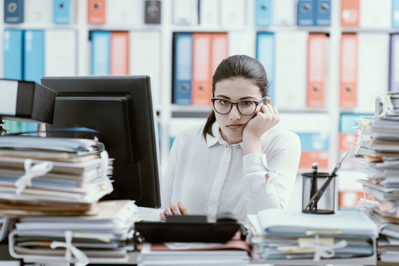 Frowning woman at desk loaded with file folders