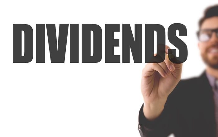 A man writing the word "dividends" on a clear board.