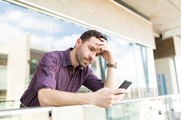 Man with worried expression holding head while looking at mobile phone