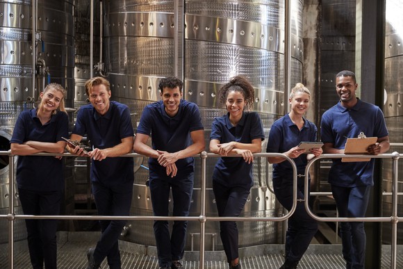 Winery staff in matching uniforms posing in front of a large steel vat.