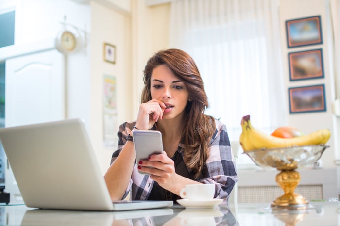 A nervous-looking woman biting her nails as she sits in front of a laptop.