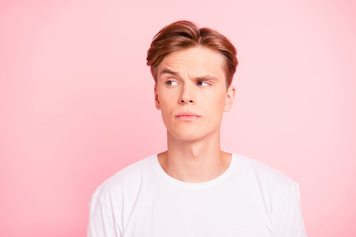 Man in white t-shirt against pink background raising an eyebrow