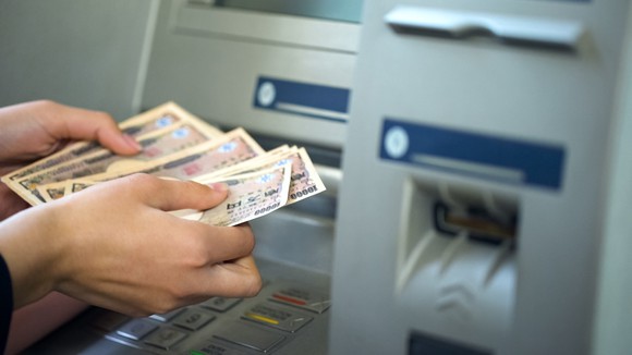 Close-up of a woman counting Japanese yen dispensed from an ATM.