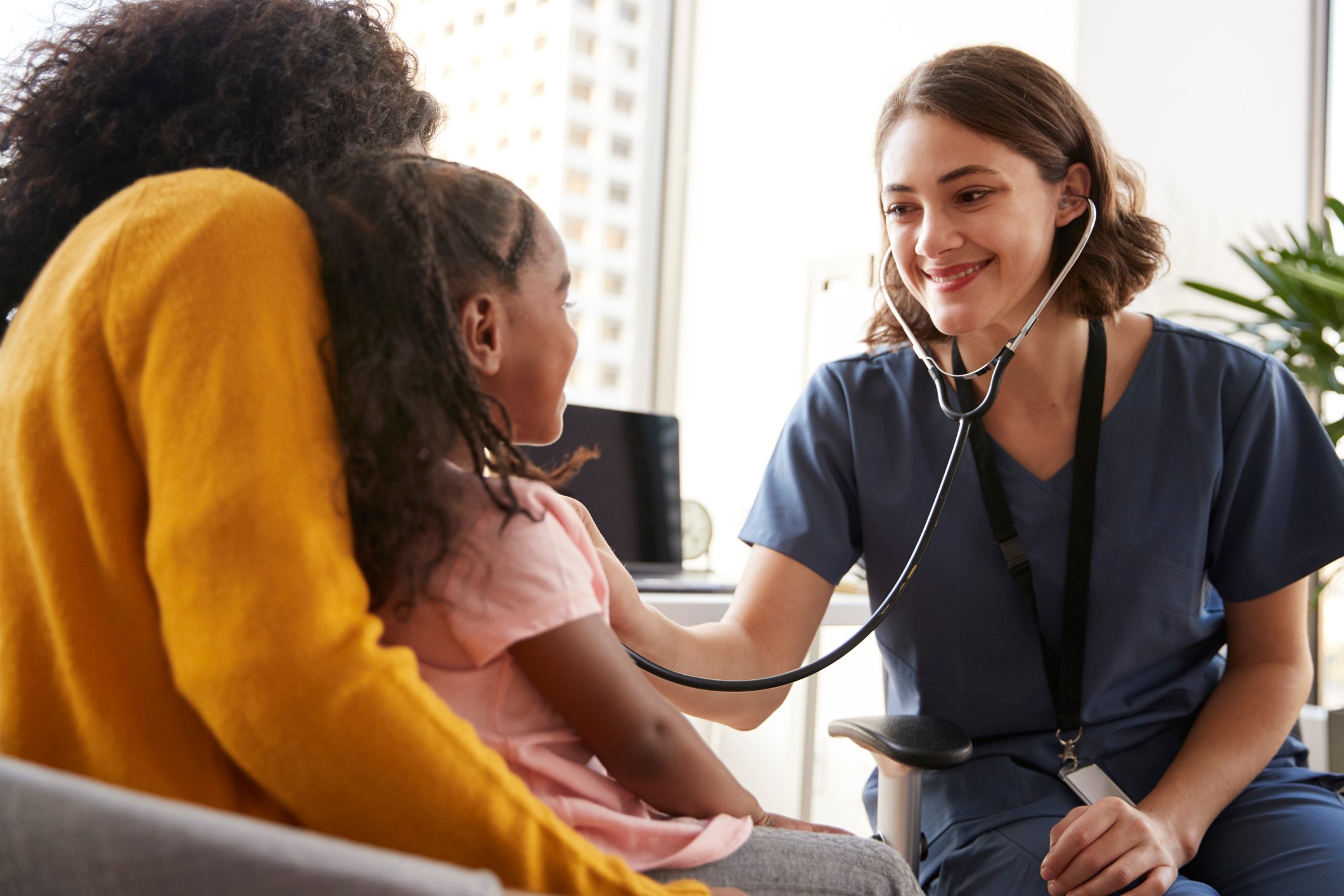 nurse using stethoscope on child who is sitting mother's lap