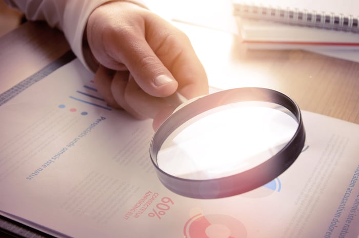 A person wearing a suit uses a magnifying glass to read a stock report.