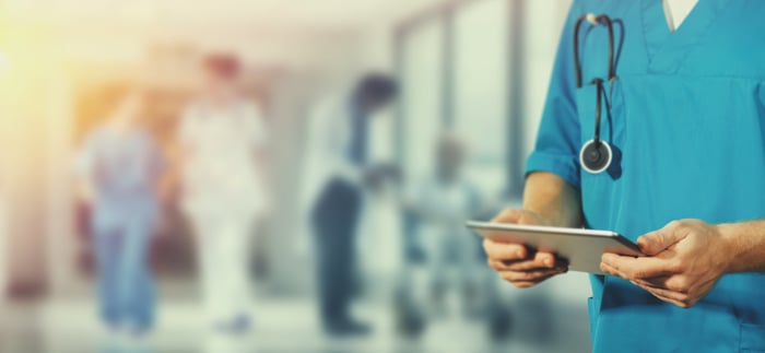 A person in hospital scrubs looking at a tablet in a hospital hallway.