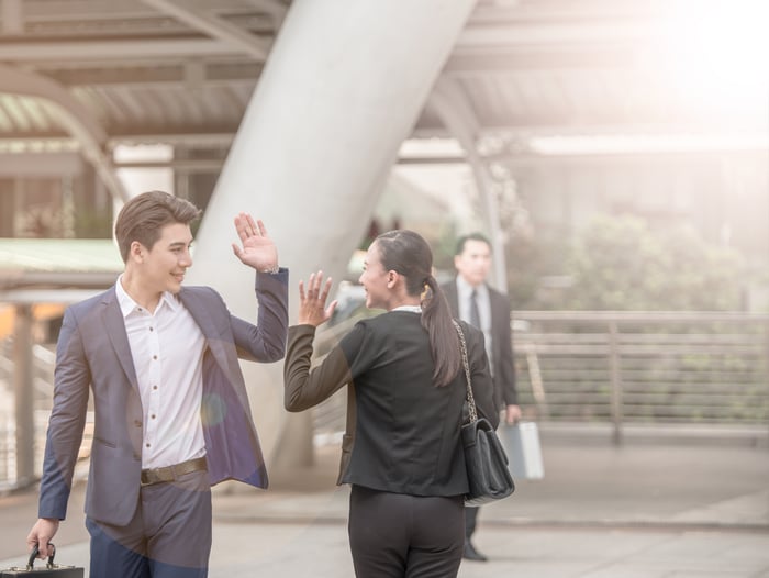 Young man in suit waving to woman in suit as he walks by