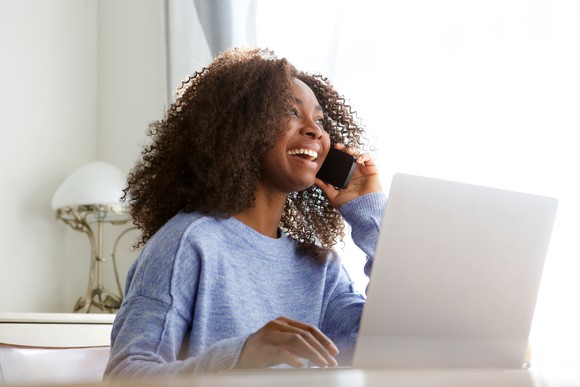 Smiling woman talking on phone while sitting at laptop.