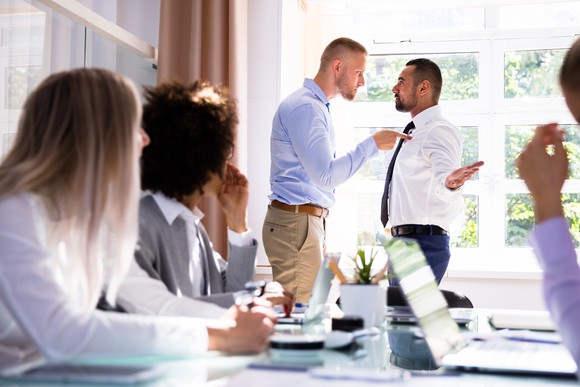 Two businessmen in a conference room arguing while others look on