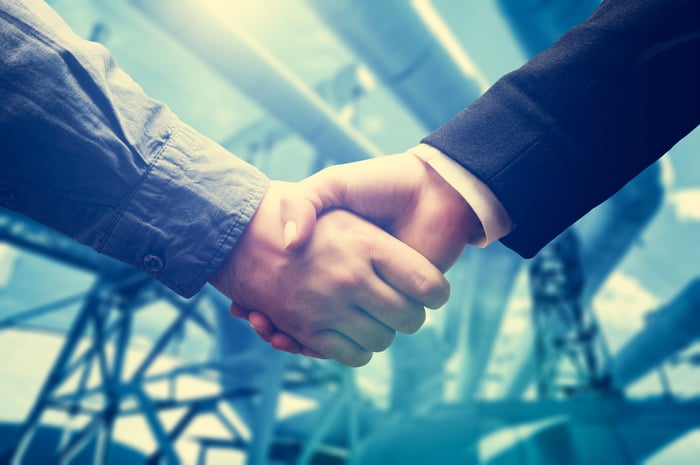 Two people shaking hands with pipelines in the background.