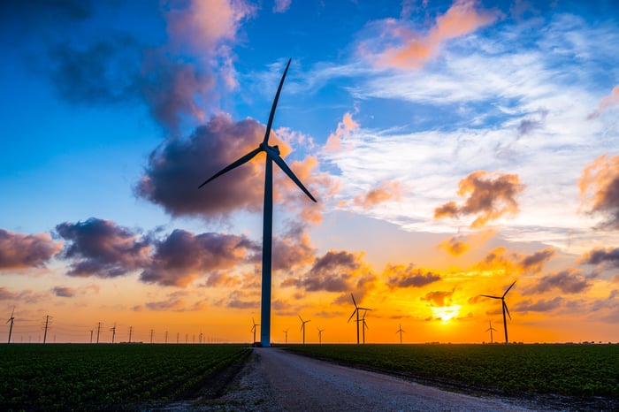 Wind turbines in a field, with the sun setting in the background.