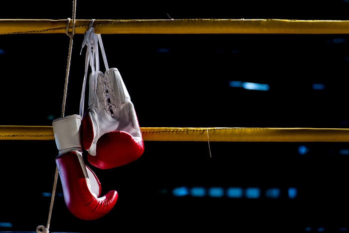 A pair of boxing gloves hanging on a rope that surrounds a boxing ring.