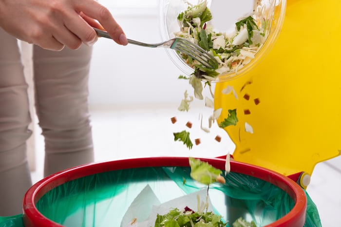 Woman throwing salad into a trash can