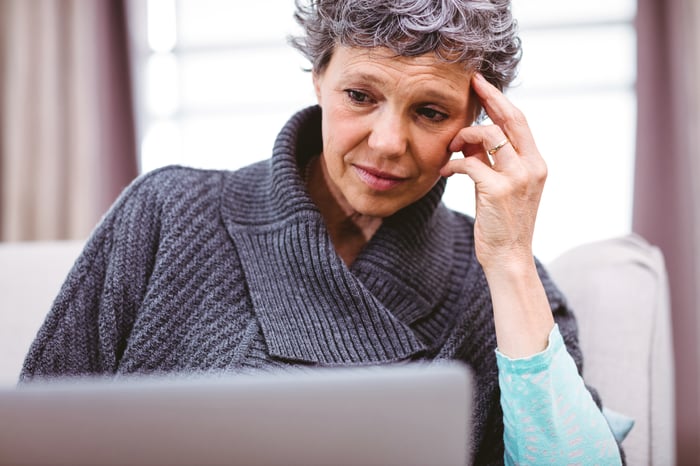 Older woman, with her hand on her temple, looking at her laptop.