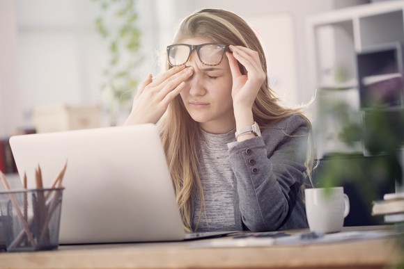 Woman sitting at laptop lifting eyeglasses to rub her eyes.