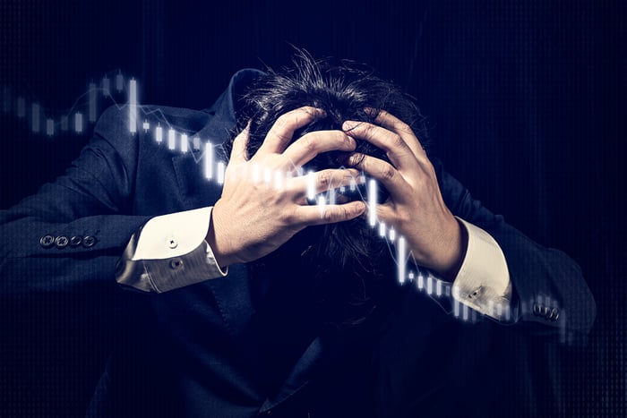 A man holding his head with a candlestick chart heading lower superimposed on top