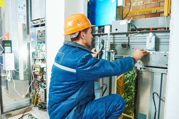 An electrician works on repairing an elevator lift mechanism.
