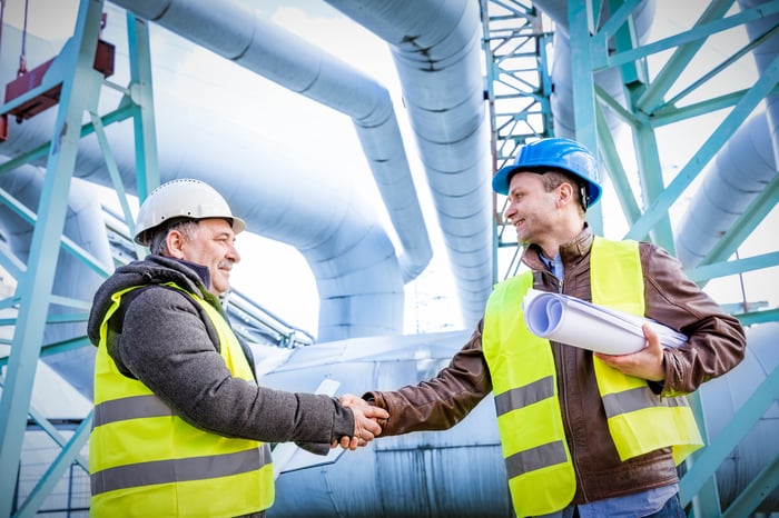 Two men shaking hands in front of energy infrastructure