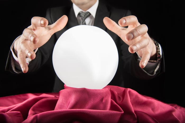 A fortune teller wearing a suit with his hands above a crystal ball.