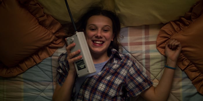 A teenage girl laying on a bed smiling and talking into a walkie talkie.