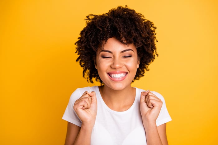 Smiling young woman, with her eyes closed, standing against a yellow background