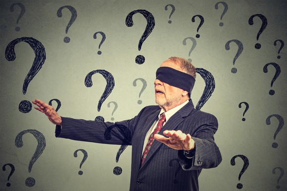 A blindfolded older businessman walks with hands outstretched, surrounded by question marks.