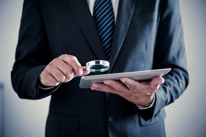 Businessman holding a magnifying glass over a touchscreen tablet