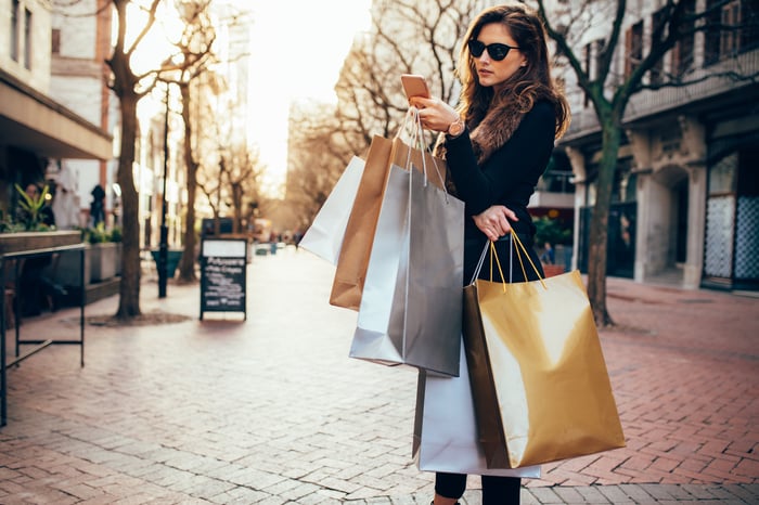 A young woman carrying shopping bags and using a smartphone.