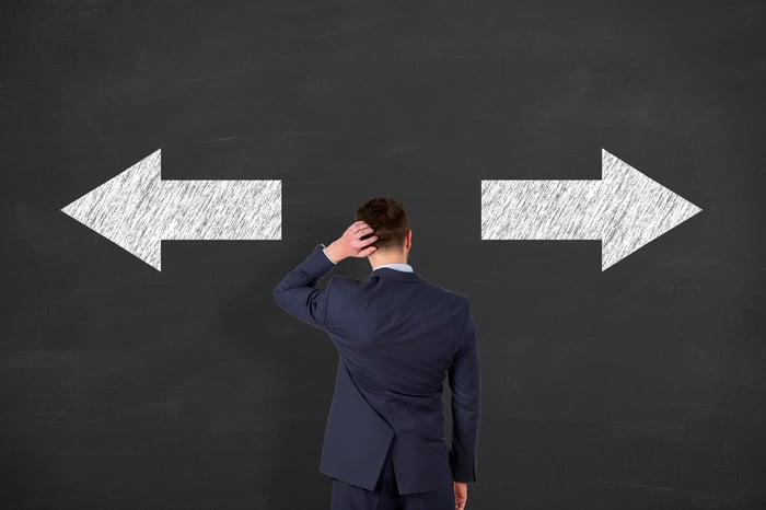 Man with hand on back of his head looking at a wall with arrows pointing left and right