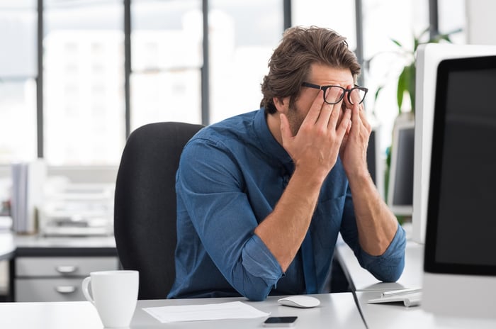 Man at computer, lifting glasses to rub eyes