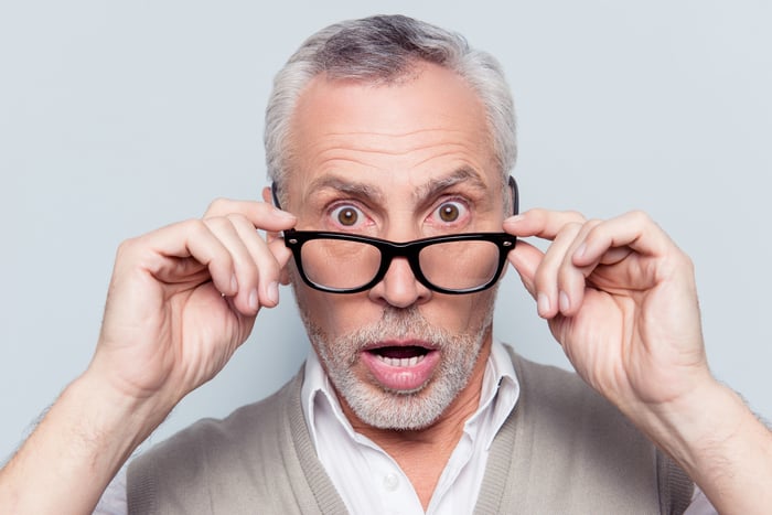 An older man looks shocked as he takes off his glasses for a closer look.