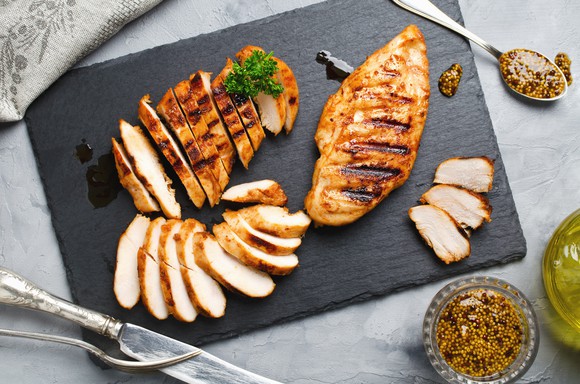 Grilled chicken on a plate surrounded by seasoning.