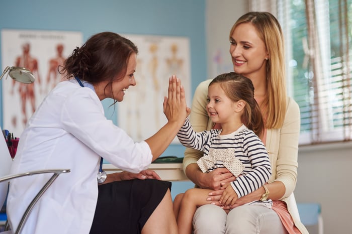 A female physician high-fiving a young child sitting on her mother's lap.