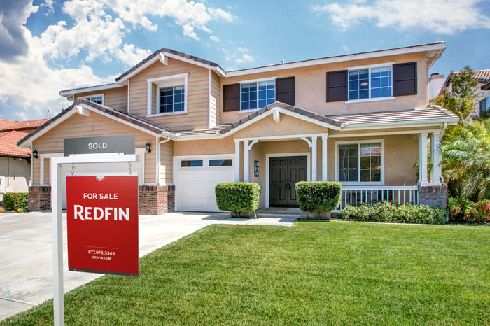 A Redfin for sale sign on the front lawn of a home, with a black sold sign attached.