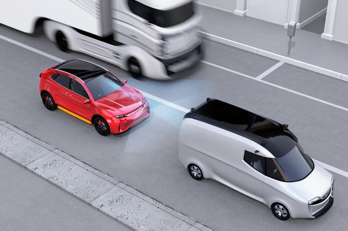 Rendering of a red car sensing an impending collision with a white van, which triggers an emergency braking action.