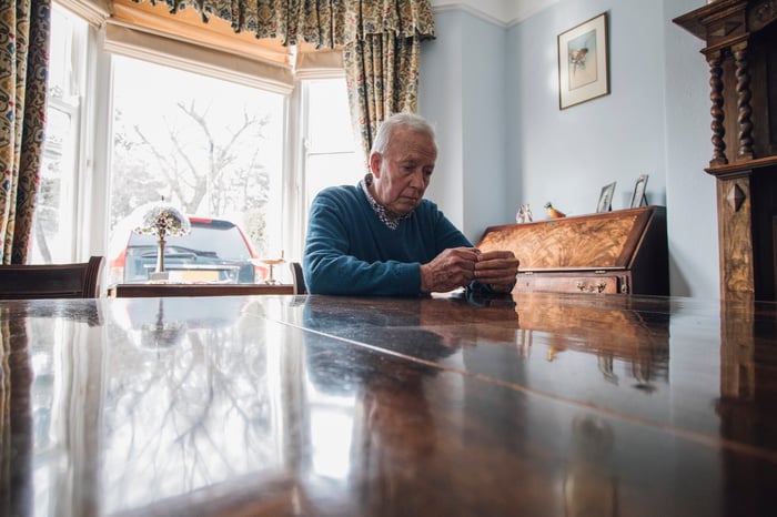 Older man with sad expression sitting at a large table