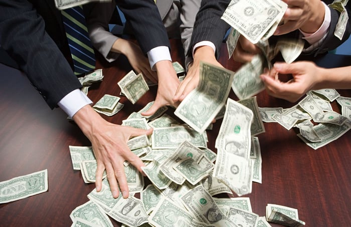 Men in suits grab money at a table.