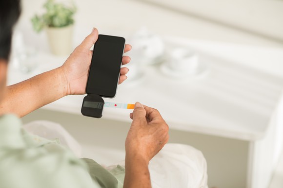 A patient measuring their blood glucose level with a add-on attached to their phone.
