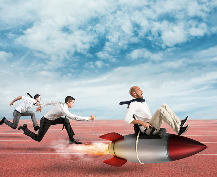 Three men racing in business attire with one tied to a rocket