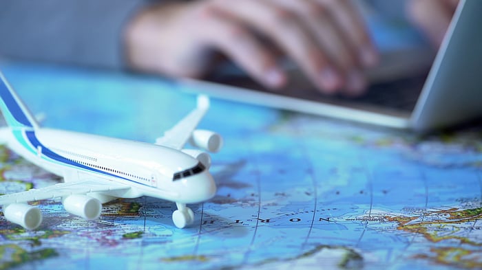 A model airplane sits on a map while a person types on a laptop in the background.