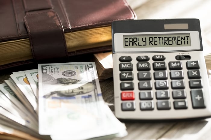 Calculator sitting next to a stack of bills with the words early retirement on its screen