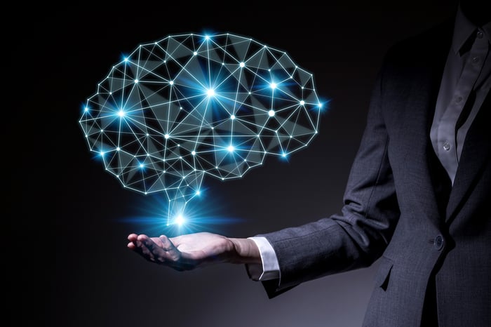An image of a human brain, outlined by lighted neural networks, shown floating above a person's hand on an outstretched arm. Concept for AI.