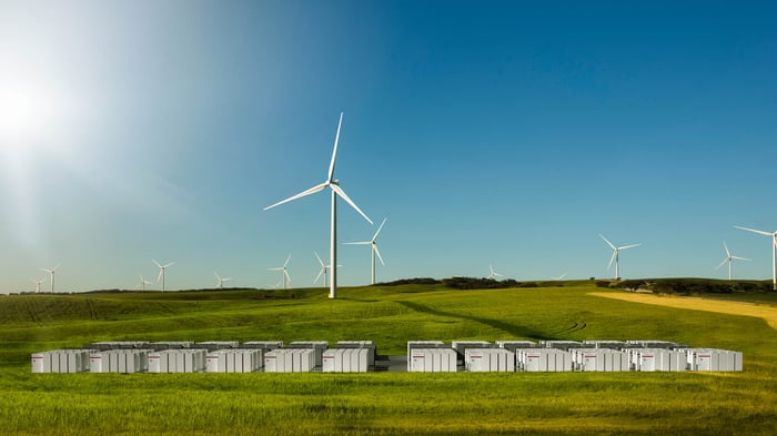 Tesla Big Battery electricity warehouse in a field in foreground and windmills in the background