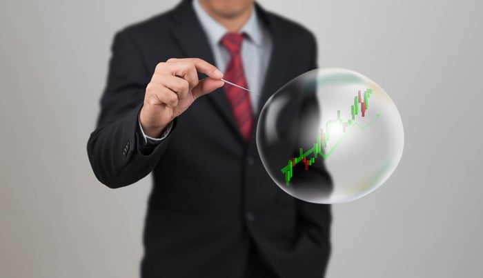Businessman holding a needle close to a bubble with a stock chart inside it.