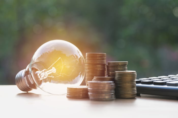 A light bulb next to stacks of coins and a calculator.