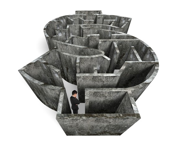 Maze shaped like a dollar sign with a man standing in it with folded arms and head looking down