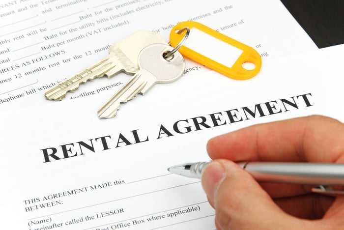 A right hand signing a rental agreement, with a set of keys on top of it.