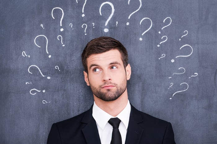 Man in business suit, eyebrow raised, with question marks surrounding his head