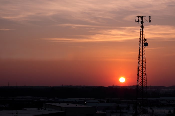 A cell phone tower with the sun setting in the background.