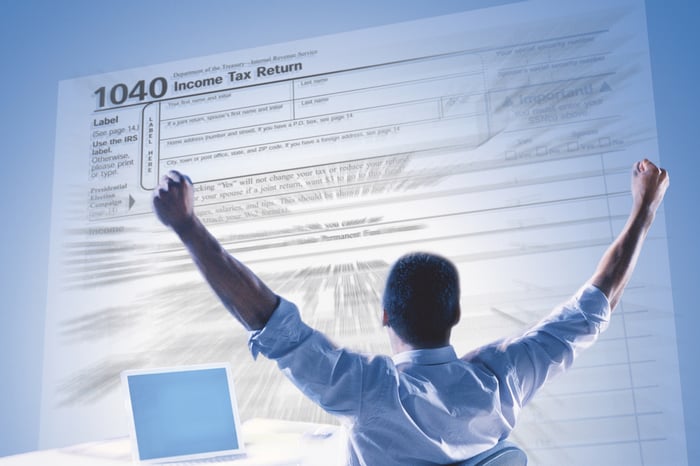 We see the back of a man raising hands in excitement, in front of a projection of a 1040 tax form.
